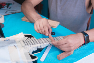 Black electric guitar in repair shop with the hands of a guitar luthier fixing it, frets alignment.