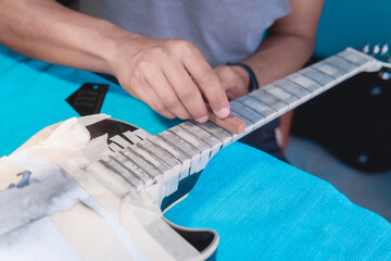 Black electric guitar in repair shop with the hands of a guitar luthier fixing it, frets alignment.