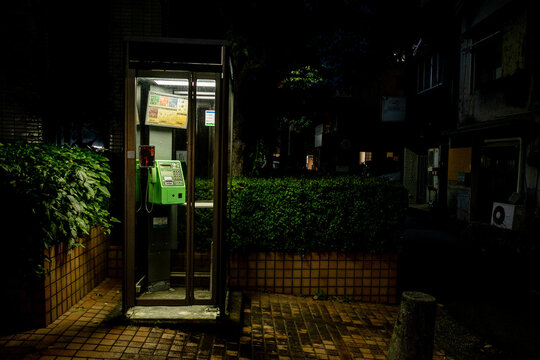 A typical japanese green coin-operated public telephone inside a booth at night at Numazu, Shizuoka.