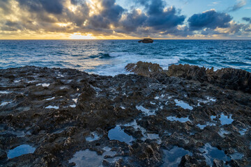 Sunrise at the rocky beach in Laie, Hawaii as clouds float in and waves crash.