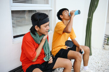 Naklejka premium Tired Two Asian Man Resting After Ping Pong Match With Drinking Water And Wiping Face By Towel