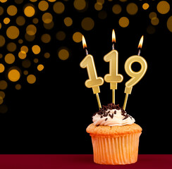 Birthday candle with cupcake - Number 119 on black background with out of focus lights