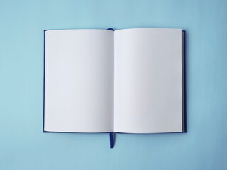 Open empty white paper book laying on blue desk, top view flat lay