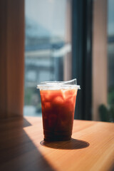 Closeup of takeaway plastic cup of iced Americano on wooden table with sun lighting