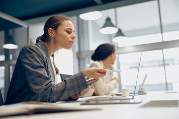 Pretty female freelancer working on laptop while sitting in modern coworking. Distance work concept