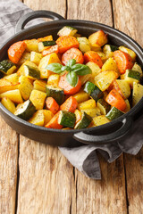 Fried potatoes with carrots, zucchini and garlic close-up in a frying pan on a wooden table. Vertical
