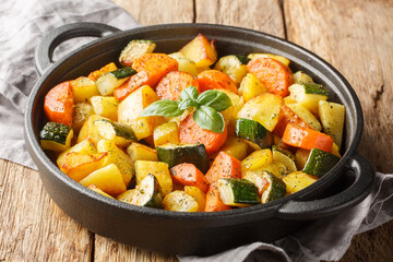 Rustic simple food fried vegetables potatoes, carrots, zucchini and garlic close-up in a frying pan...