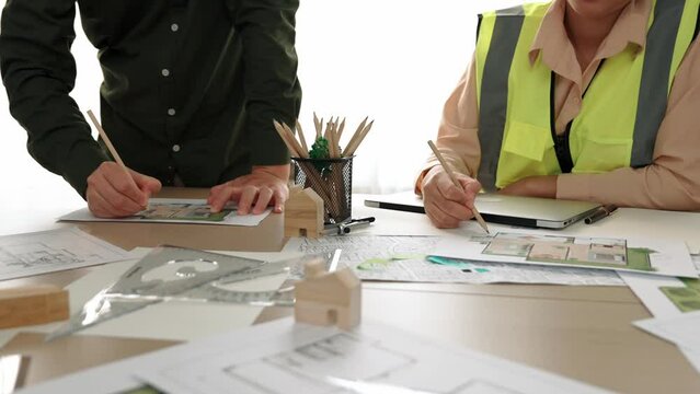 Smart architect and safety engineer discussion about building blueprint on table with architectural document, measurement tools and wooden block scatter around at modern office. Closeup. Delineation.