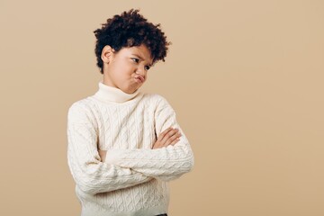 Frustrated young african american girl standing with arms firmly crossed, expressing determination against neutral beige background