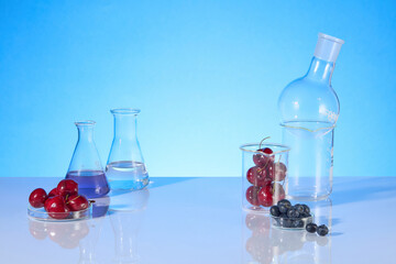 Template for designing over blue background from front view, on both sides decorated with experiment utensils, which contain ripe cherry, blueberry and extract from it. Blank space for designing