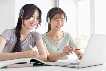 Happy young girls with wireless headphones  reading listening online courses, studying remotely from home