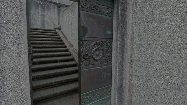 Frist person view walking through old, richly decorated metal doors and up the stone stairs of a historical monument. Entering  Wrigley Memorial on Santa Catalina island in the rain.                 