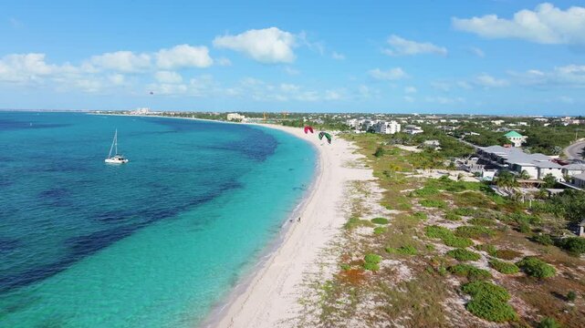 Forward aerial 4K footage of Grace Bay coastline with parasailing activities, a boat on lively blue ocean waters, and green land on the right.
