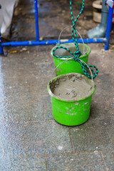 A plastic bucket filled with cement, roped for hoisting to a construction site above