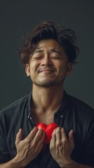 A man with his eyes closed holds a red heart to his chest