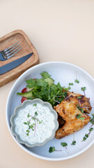 Delicious fried chicken wings with yogurt sauce and greens top view on beige background