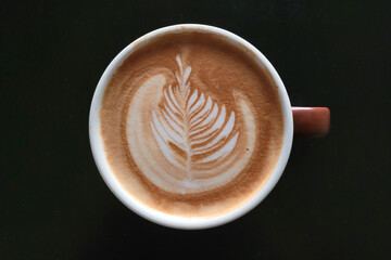 Top-down view of a coffee cup with latte art on a black table background
