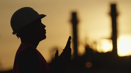 A man in a hard hat and safety vest is holding a walkie talkie. The image has a mood of seriousness and caution, as the man is likely working in a hazardous environment