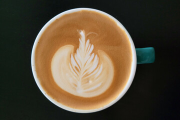 Top-down view of a coffee cup with latte art on a black table background