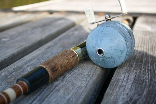 Close-up of a vintage fishing rod and reel resting on a wooden d