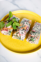 Close-up of fresh spring rolls on a yellow plate with a mint garnish