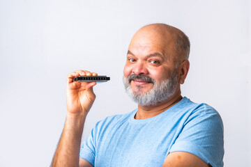 Indian asian senior old elderly man plays harmonica or mouth organ against white