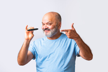 Indian asian senior old elderly man plays harmonica or mouth organ against white