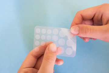 Close-up round acne patch on finger on blue background. Acne patches for treatment of pimple and...