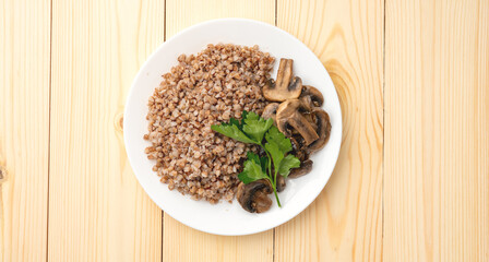 Buckwheat porridge with fried mushrooms on a plate on a wooden background. A green leaf decorates the dish. Healthy diet food. The concept of healthy eating.