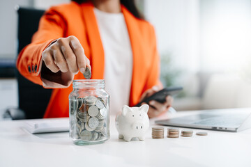 businesswoman holding coins putting in glass with using smartphone and calculator to calculate...