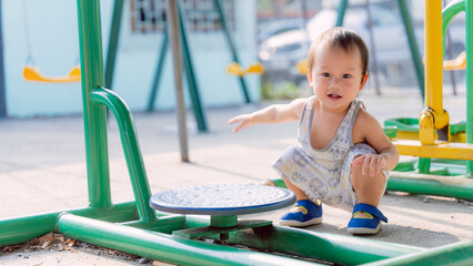 Portrait of smiling Asian boy squatting and playing with rotating plate on exercise machine at...