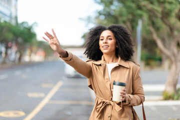 Confident Businesswoman Hailing a Taxi While Holding a Coffee Cup on a City Street
