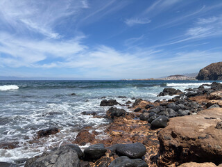 View from a rocky beach of the Atlantic ocean in Tenerife, waves splashing on the beach, horizon over water and profile of La Gomera island. Travel, vacation concept