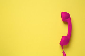 Magenta telephone handset on yellow background, top view. Space for text