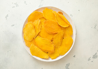 Round plate with dried mango pieces on light background.