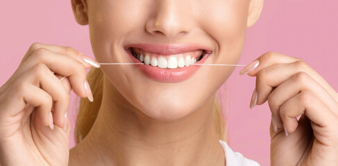 A close-up of a woman flossing her teeth with white floss. Her mouth is open and she is smiling,...