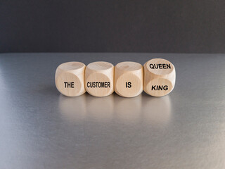 Turned a wooden cube and changes the slogan 'the customer is king' to 'the customer is queen'. Beautiful black background, gray table. Business concept.
