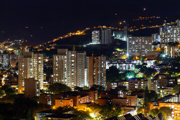 Obraz premium Panoramic view (cityscape) of Medellin by night, Antioquia, Colombia. Enlightened residential buildings and condominiums. Urban jungle.