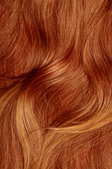 Red hair close-up as a background. Women's long orange hair. Beautifully styled wavy shiny curls. Hair coloring bright shades. Hairdressing procedures, extension.