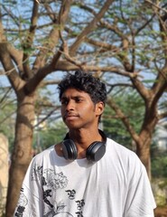 Stylish young man wearing headphones around his neck in the park with good nature trees background 