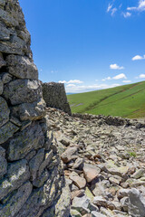 Close view of stone wall and towers of Abuli prehistoric fortress. Huge rocks around. Hill covered with green grass