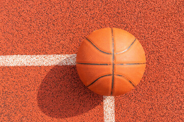 Basketball ball on the ground. Close-up ball on the red court. Basketball on the street or indoor court. Sports gear without people. Minimalism. Template, sport background 