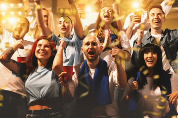 Crowd of sport fans cheering during match on stadium. Excited people standing raised arms ,...