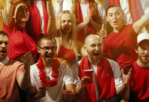 Group portrait of emotional people, fans standing on tribunes and loudly shouting to support their team. People in scarfs with drinks. Concept of sport, competition, support, world, cup. Ad
