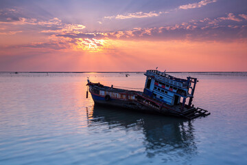 A fishing boat is broken or abandoned in the middle of the sea at sunset in Chonburi, Thailand.