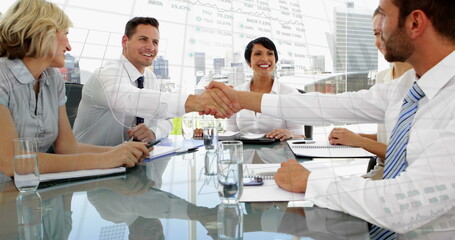 Image of graphs and trading board over diverse coworkers shaking hands after meeting