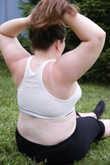 Young woman plus size in sport wear effort doing exercise on the grass outdoor. Girl is stretching....