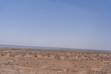 A desert landscape with a blue sky and a few trees in the distance. The sky is clear and the sun is shining brightly