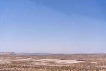 A vast, empty desert with a clear blue sky above. The sky is so clear that it almost looks like a painting