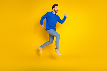 Fototapeta na wymiar Full length photo of handsome young guy fast running dressed stylish blue garment isolated on yellow color background